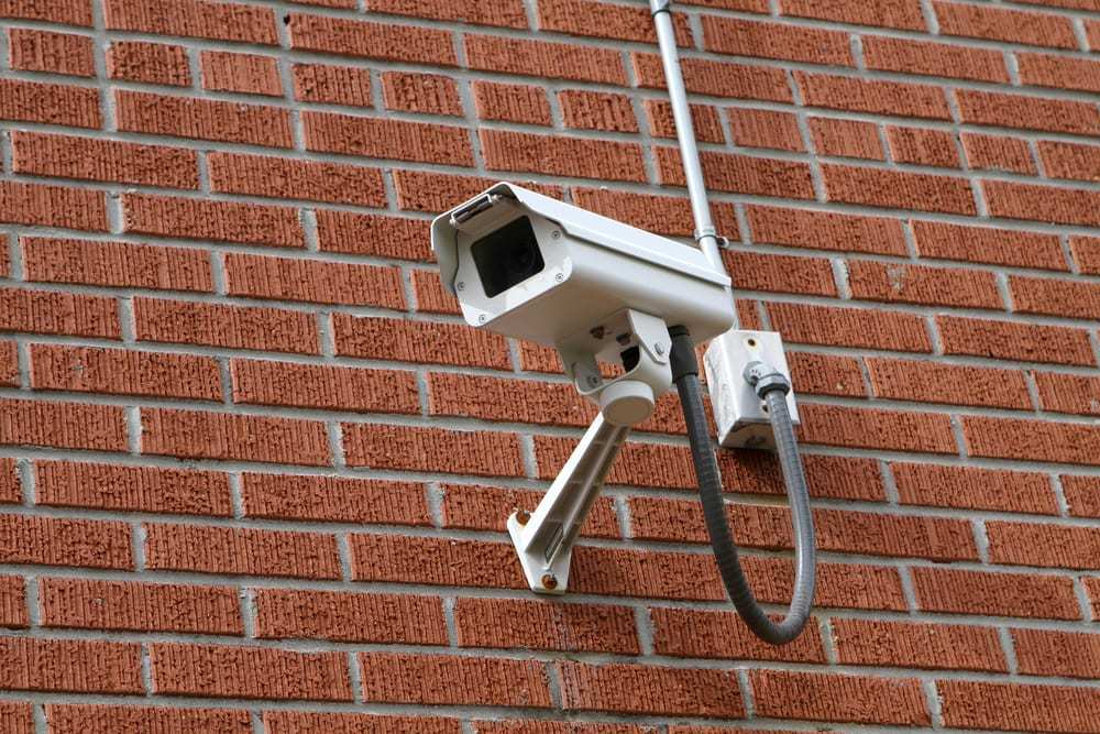 Surveillance video camera mounted to a brick wall outside a building for security